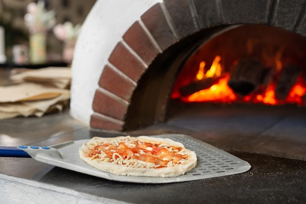 Italian pizza is cooked in a woodburning oven The cook puts the pizza in the oven on a shovel