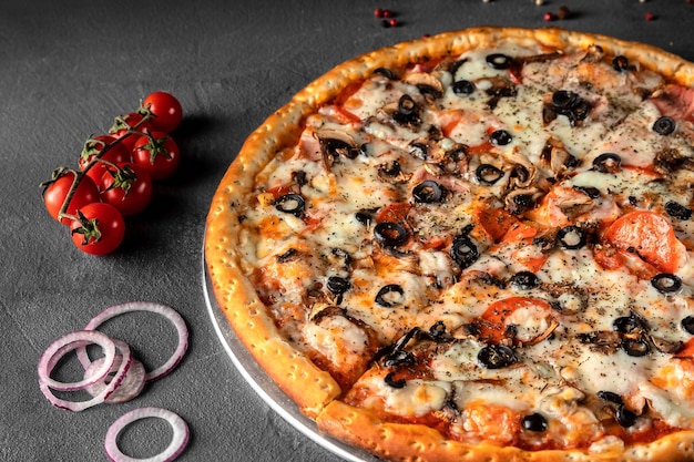 Italian pizza with cheese, olives, tomato, onion, pepperoni sausage on a gray table, close-up