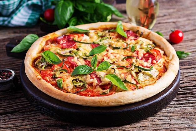 Italian pizza with chicken, salami, zucchini, tomatoes and herbs on vintage wooden background.  Italian cuisine