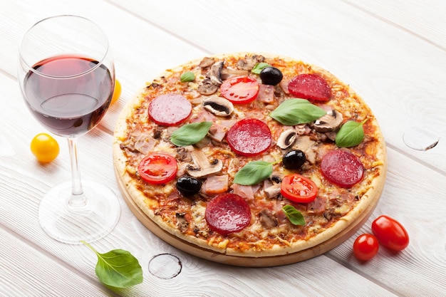 Italian pizza with pepperoni tomatoes olives basil and red wine