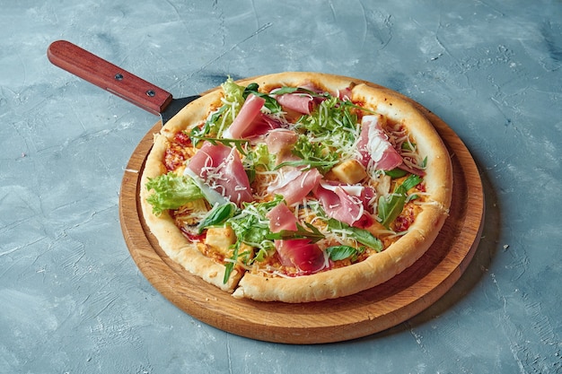 Italian pizza with prosciutto, parmesan, lettuce and cheese on a wooden board on a gray surface