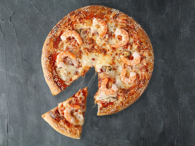 Photo italian pizza. with tiger prawns, squid, mussels, tomato sauce, mozzarella cheese. a piece is cut off from pizza. view from above. on a gray concrete background. isolated.