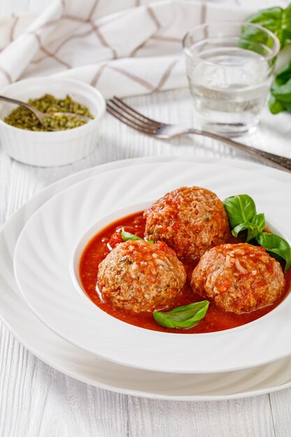 Photo italian porcupine balls ground beef and rice meatballs in tomato sauce with basil leaves in white bowl on white wooden table vertical view from above