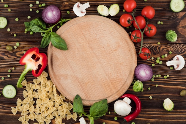 Italian products near round wooden board surrounded by cherry tomatoes and garnished with greens, pasta, peper