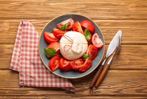 Photo italian salad with fresh tomatoes, burrata cheese, basil and olive oil served on ceramic plate on rustic wooden background from above, healthy snack or lunch