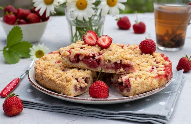 Italian sbricholata pie with shortcrust pastry and strawberries on a gray table with a bouquet of daisies Still life in an open space