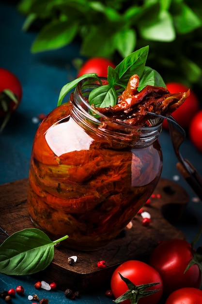 Italian Sun Dried tomatoes in olive oil with green basil and spices in glass jar on blue kitchen....