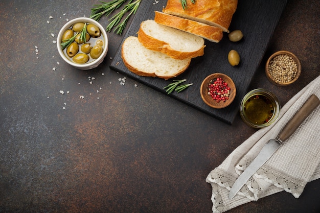 Italian traditional Ciabatta bread with olives, olive oil, pepper and rosemary on a dark concrete surface