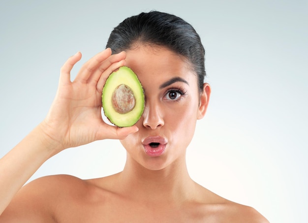 Its an all round nourisher Studio portrait of a beautiful young woman covering her eye with an avocado against a gray background