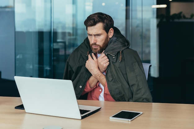 Its cold in the office the businessman is freezing while working on a laptop inside the building the