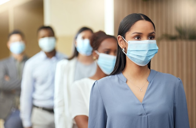 Its a question of health and safety Cropped shot of an attractive young businesswoman wearing a mask while standing at the head of a queue in her office