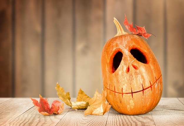 JackoLantern Pumpkin and autumn leaves on wooden background