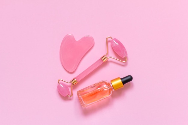 Jade facial roller and essential oil on a pink background Top view a place to copy Facial Massage With Rose Quartz