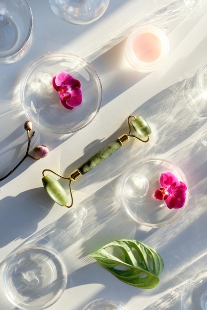 Jade stone face roller with monstera leaf orchid flowers and glass baubles pink moisturizer cream