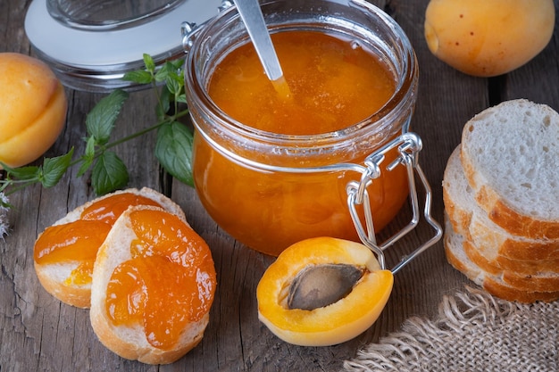 Jam from apricots in a glass jar and bread on an old wooden table