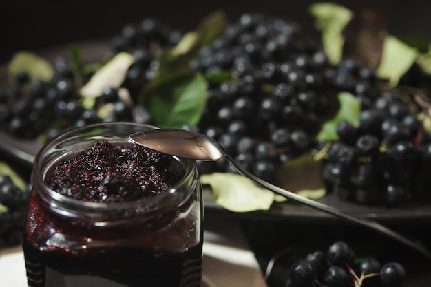 Jam from black chokeberries and its berries on dark table.