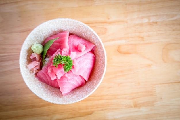 Japan food Tuna or Maguro don Consisting of sliced Tuna or Maguro on top of Japanese rice Served with wasabi and pickled ginger in a white bowl on a wooden table.