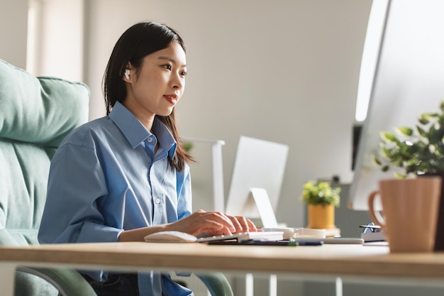 Japanese Business Lady Using Computer Wearing Earbuds Typing In Office