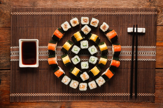 Japanese food art. Delicious uramaki rolls set, colorful round ornament of sushi served on brown straw mat, flat lay. Luxury restaurant menu photo.