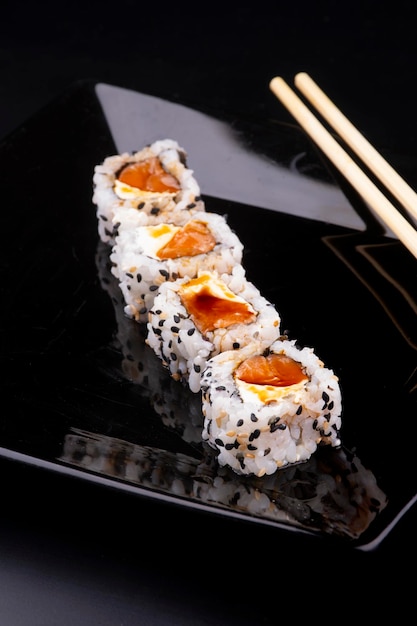 Japanese food on black plate with 4 more salmon and cream cheese sushi with soy sauce and chopsticks in closeup angle