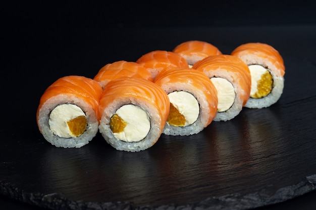 Japanese food, rolls with salmon, philadelphia curd cheese and orange on black background.