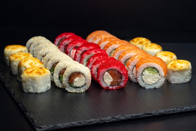 Japanese food, set of baked rolls, rolls in white sesame, red tobiko caviar, Philadelphia with curd cheese on a black slate board.