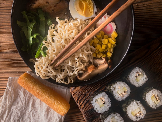 Japanese food. Traditional Ramen bowl and sushi maki in wooden table, flat lay.