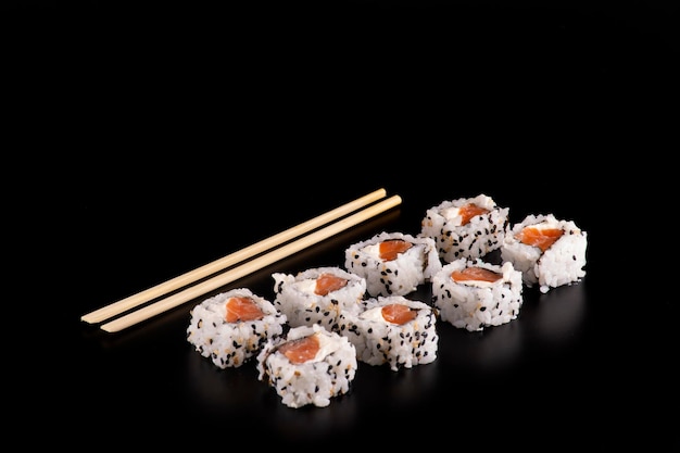 Japanese food in with four side by side salmon sushi rolls and cream cheese and chopsticks seen almost from above