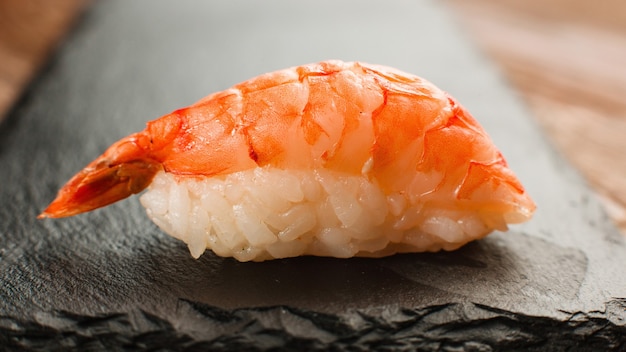 Japanese healthy food, national cuisine. One shrimp sushi nigiri with delicious prawn served on black slate, closeup view.