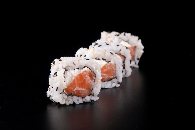 Japanese oriental food in with four side by side salmon sushi rolls and cream cheese viewed in front row on black background in close up portrait blurred background