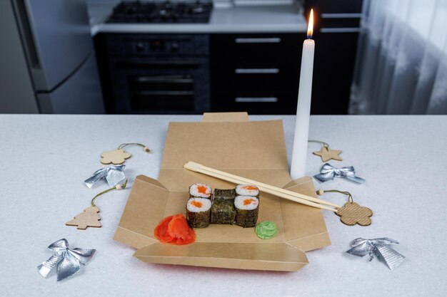 Japanese rolls with red fish in an open cardboard box on the table Table decoration in a festive style Christmas toys and a candle