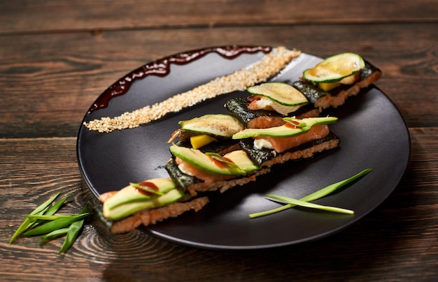 Japanese sandwich rolls serving with sesame teriyaki sauce Raw fish avocado and salad on black plate Top dark view