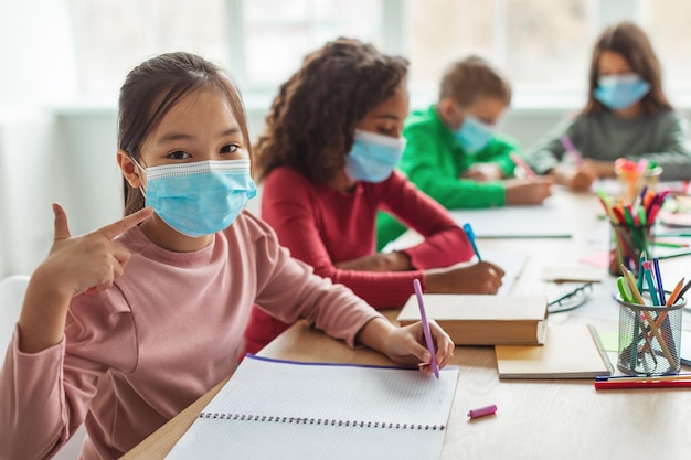 Japanese Schoolgirl Wearing Face Mask Gesturing Thumbs Up In Classroom