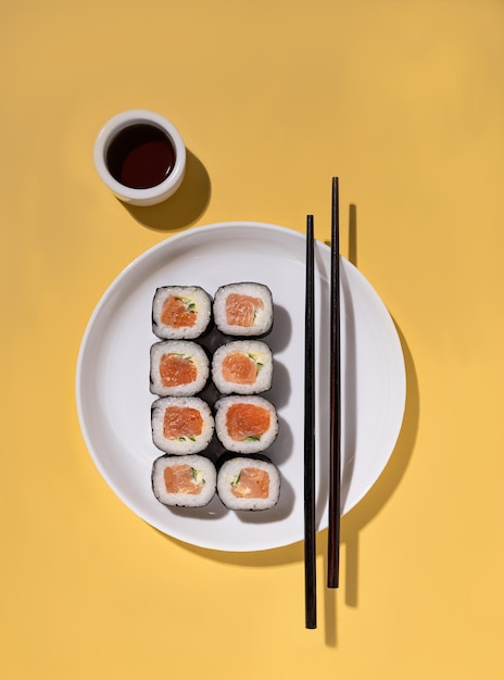 Japanese Sushi roll with salmon cucumber and soy sauce with chopsticks in the white plate on yellow background with hard shadow Concept food photography Top view and copy space