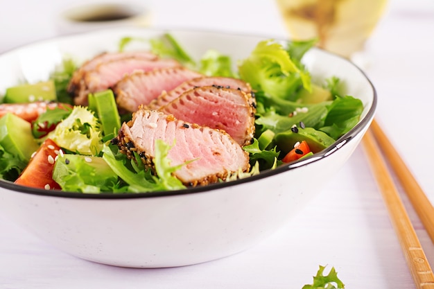  Japanese traditional salad with pieces of medium-rare grilled Ahi tuna and sesame with fresh vegetable on a bowl. 