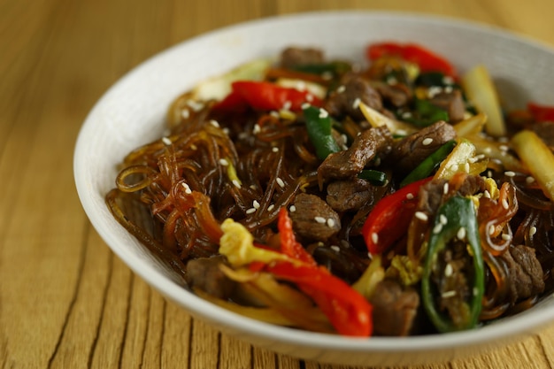 Japchae Korean Glass noodle stir fry Served in the bowl with wooden background