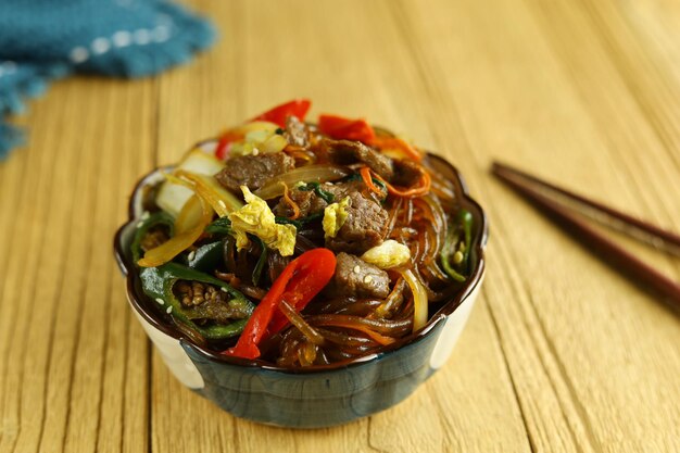 Japchae Korean Glass noodle stir fry Served in the bowl with wooden background