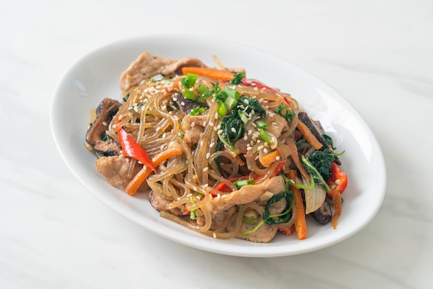 japchae or stir-fried Korean vermicelli noodles with vegetables and pork topped with white sesame - Korean traditional food style