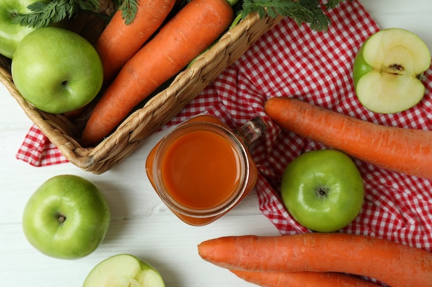 Jar of apple carrot juice and ingredients on white wooden isolated background