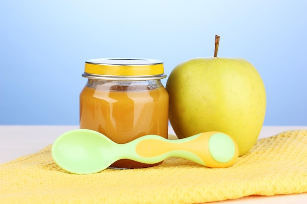 Jar of baby puree with spoon on napkin on blue background