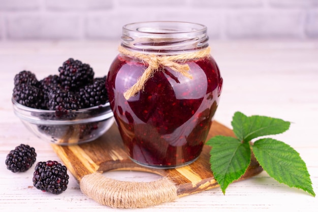 A jar of blackberry jam on a white wooden background.