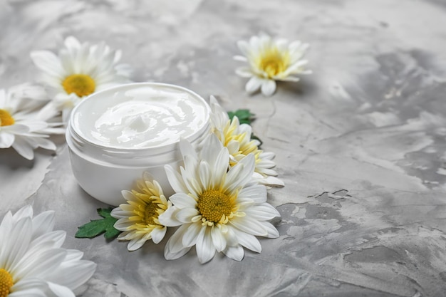 Photo jar of body cream and flowers on grey background