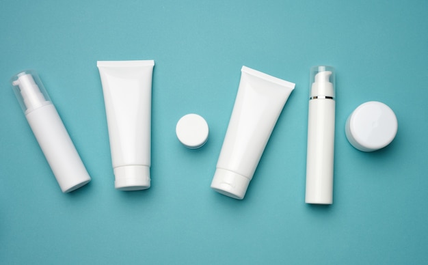 Jar, bottle and empty white plastic tubes for cosmetics on a blue background. Packaging for cream, gel, serum, advertising and product promotion, mock up