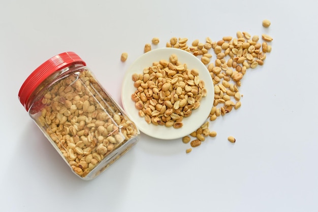 Jar and a bowl of roasted peanuts on a white surface