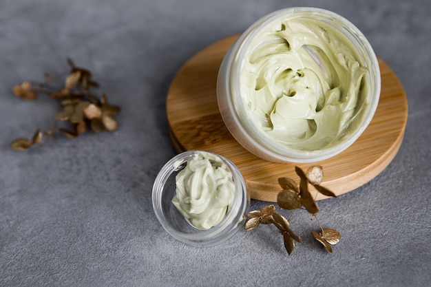 A jar of face cream on a wooden stand on a gray table. Set for skin and body care beauty products