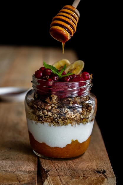 Jar of homemade granola with yogurt, homemade apricot jam and raspberries on dark 