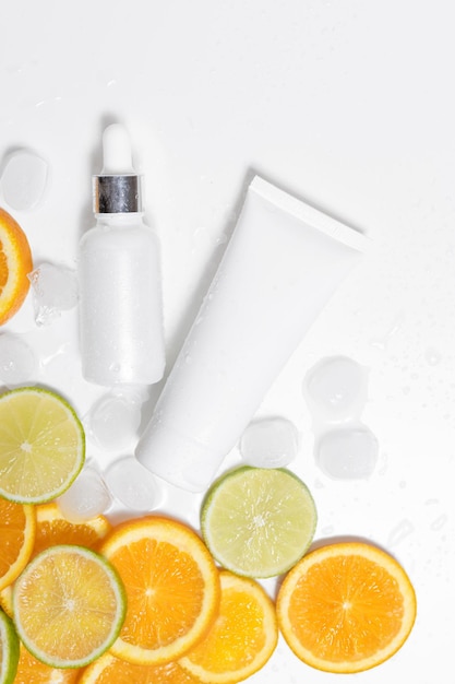 A jar of serum and cream with citrus lies in ice on a white isolated background place for your design