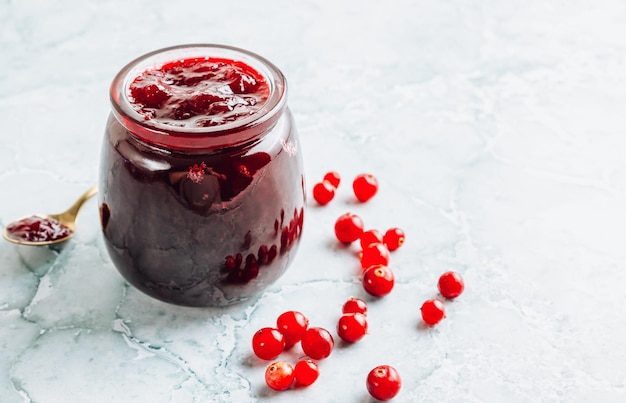 Jar of tasty cranberry jam on light marble background