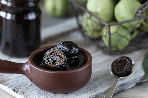 Jar of walnut jam on a wooden table and a group of green walnuts.