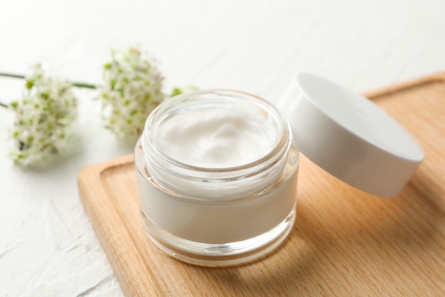 Jar with cream, allium flowers and board on white background